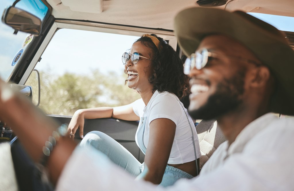 A couple laughs in their car on a road trip.