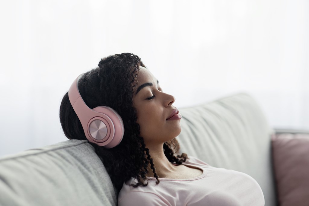 Closeup shot of a black woman leaning back with her eyes closed with pink headphones on.