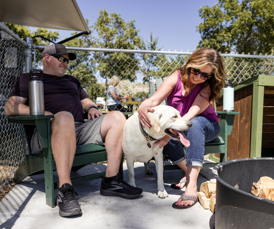 A man, woman, and a dog sit in a fenced in Paw Pen site at Billings KOA Holiday